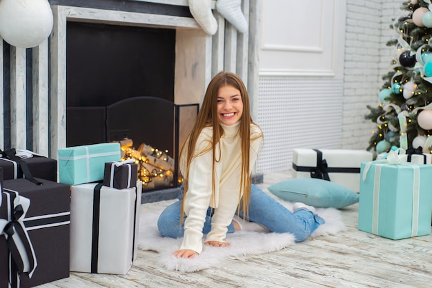 Feliz linda joven en Navidad en casa junto a la chimenea