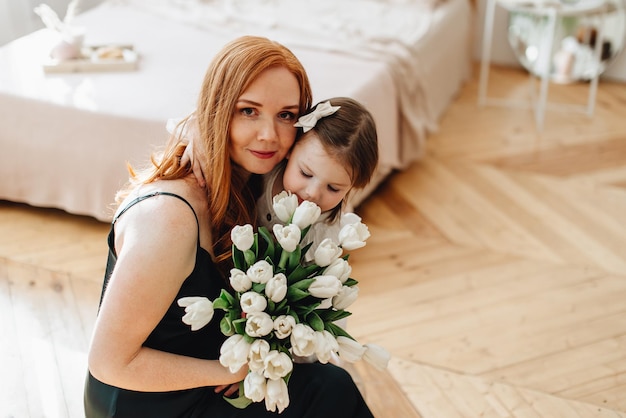 Foto feliz linda mãe carinhosa com um buquê de flores da primavera abraça sua filha em casa na cama aproveita o momento de surpresa comemora o dia das mães