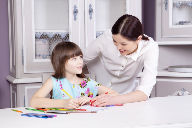 Feliz linda mãe ensina a filha a pintar, pintar, sorrir e olhar para a câmera. tiro do estúdio.