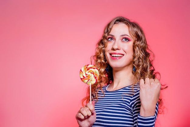 Feliz linda menina morena com maquiagem vermelha, cabelo encaracolado e um suéter de listras azuis posando contra um fundo vermelho. Foto horizontal