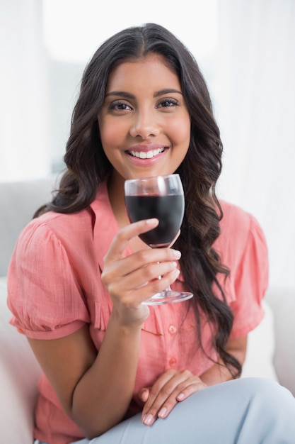 Feliz linda morena sentada en el sofá con copa de vino