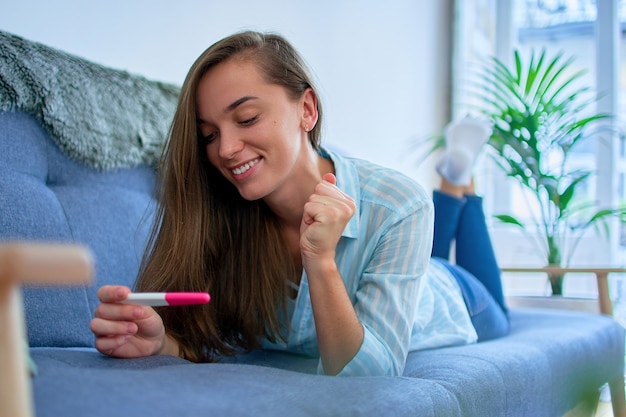 Feliz linda mujer sonriente joven satisfecha mirando la prueba de embarazo con dos rayas