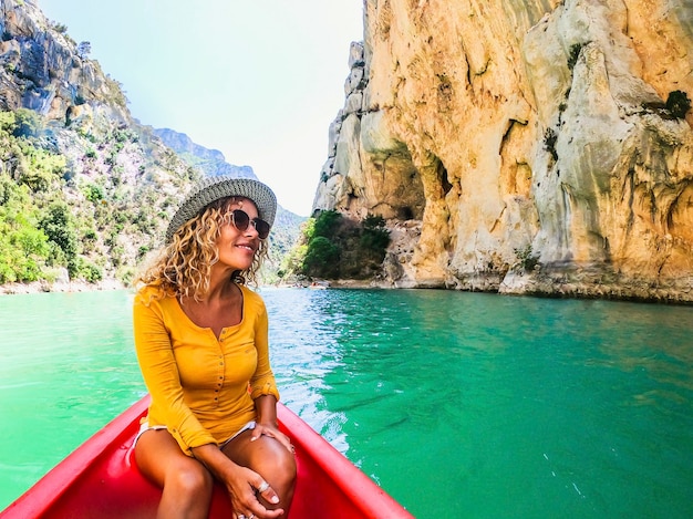 Feliz linda mulher de chapéu, desfrutando de seu passeio em uma canoa na superfície do cânion de água verde em meio a um penhasco da montanha rochosa. Turista sorridente sentada em uma canoa entre um penhasco rochoso