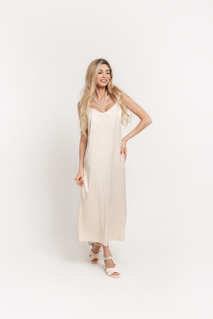 Feliz linda mulher elegante com um elegante vestido bege longo e estiloso com sapatos de salto em fundo branco no estúdio