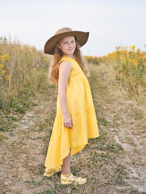 Feliz linda niña con vestido amarillo y sombrero camina en el campo