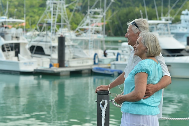 Feliz linda pareja senior en el muelle con yates