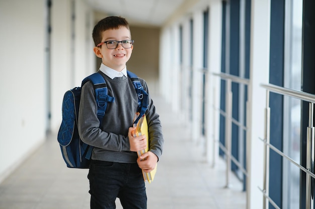 Feliz lindo chico inteligente con gafas con mochila escolar y libro en la mano Primera vez en la escuela Regreso a la escuela