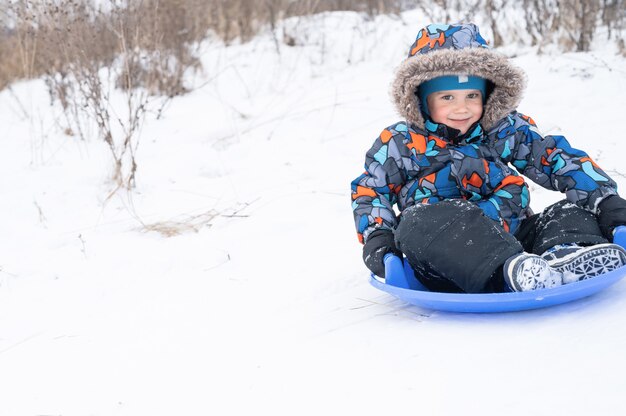 Un feliz y lindo niño de cinco años es actividad y diversión pasando sus nevadas vacaciones de invierno cabalgando por un tobogán en un trineo