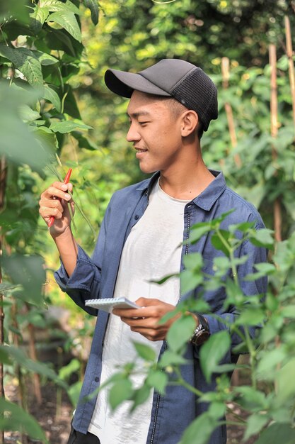 Feliz de macho joven agricultor asiático mirando los frijoles largos, en el jardín.