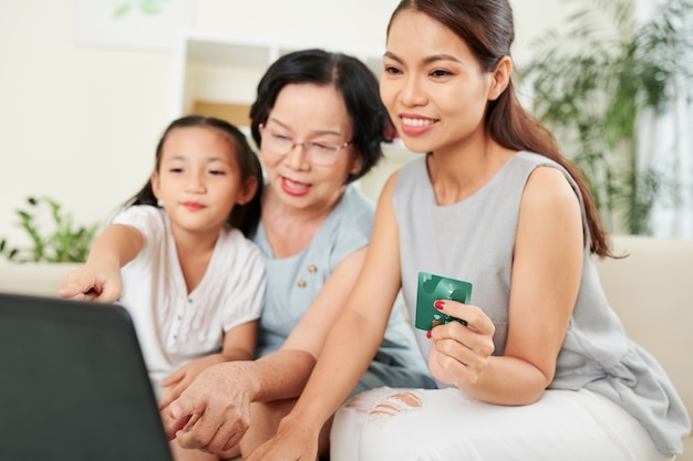 Feliz madre, abuela y niña comprando en línea juntas, pidiendo comida o ropa y pagando con tarjeta de crédito