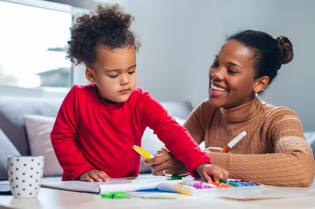 Feliz madre afroamericana ayudando a su hija a colorear