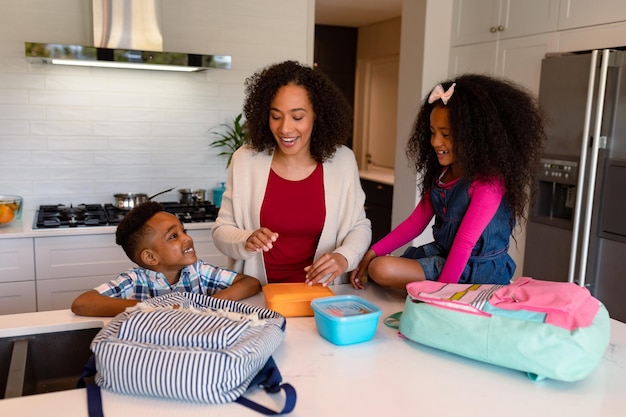 Feliz madre afroamericana e hijos preparando loncheras para la escuela