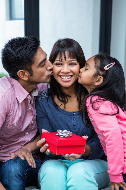 Feliz madre besada por sus hijos mientras sostiene un regalo