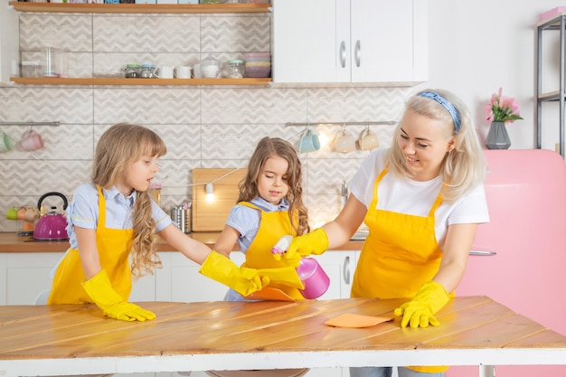 Feliz madre caucásica ayudando a sus hijas en edad preescolar a limpiar la mesa en la cocina después de cocinar