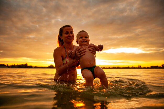 Feliz madre caucásica nadando con lindo bebé sonriente en el mar