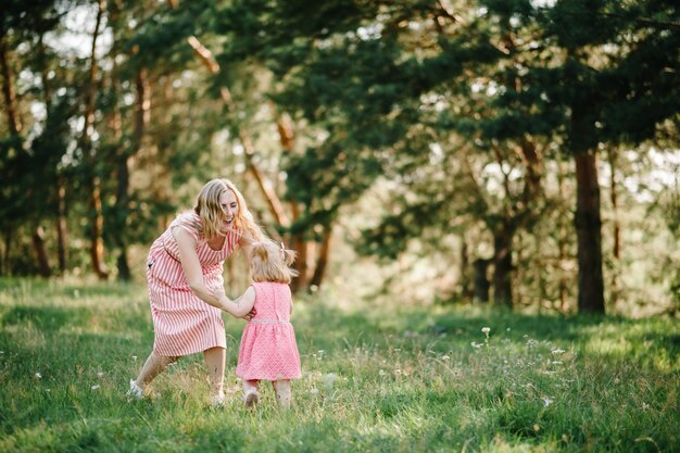 Feliz madre corre y coge a la hija con sus manos en la naturaleza en las vacaciones de verano. Mamá y niña jugando en el parque a la hora del atardecer. Concepto de familia amistosa. De cerca.