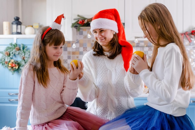 Feliz madre da a sus hijas mandarinas en cocina decorada de Navidad