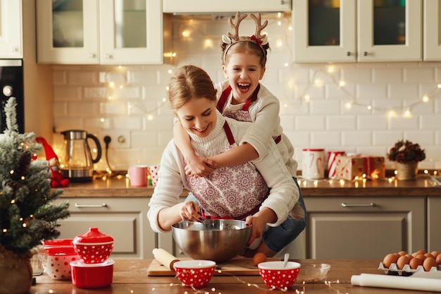 Feliz madre divertida e hija hornean galletas navideñas