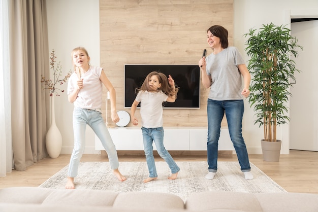 Feliz madre y dos hijas que se divierten cantando canciones de karaoke en cepillos para el cabello.