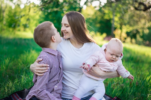 Feliz madre con dos hijos. Hermano y hermana con momia en el parque. Mamá abraza a su hijo y sostiene al bebé