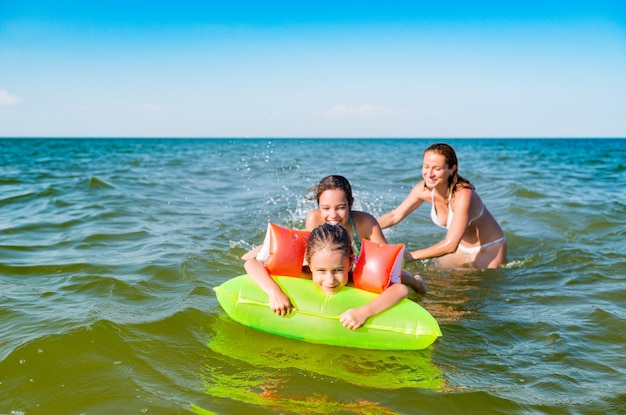 Feliz madre y dos pequeñas hijas positivas se bañan y nadan en el mar con un colchón de aire en un día soleado de verano. Concepto de vacaciones con niños. Copyspace