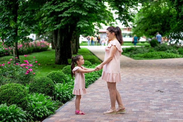 Feliz madre e hija de 5 a 6 años caminan por el parque en verano, la madre habla con su hija, el concepto de una familia feliz, la relación de madre e hijo