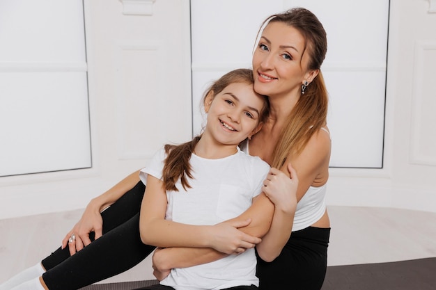 Feliz madre e hija abrazándose en ropa deportiva en el gimnasio