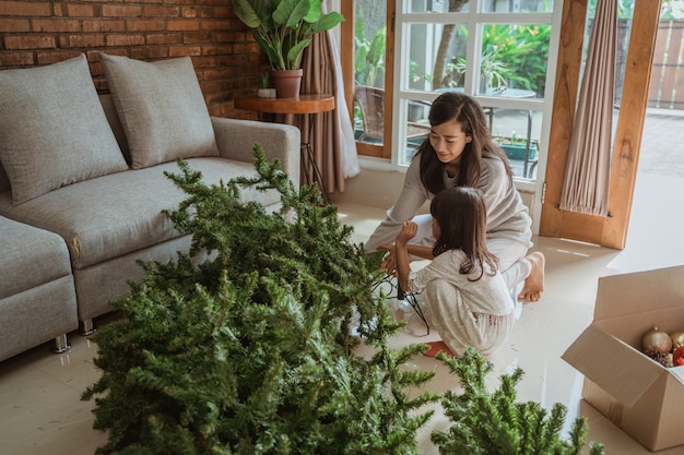 Feliz madre e hija asiáticas decorando el árbol de Navidad