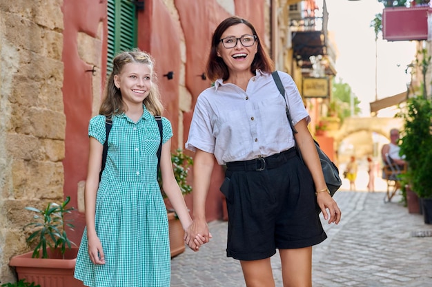 Feliz madre e hija caminando juntos cogidos de la mano por las calles de la ciudad