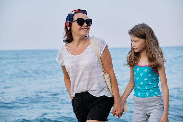 Feliz madre e hija caminando juntos en la playa cogidos de la mano. Familia, vacaciones, estilo de vida, amor, concepto de fin de semana