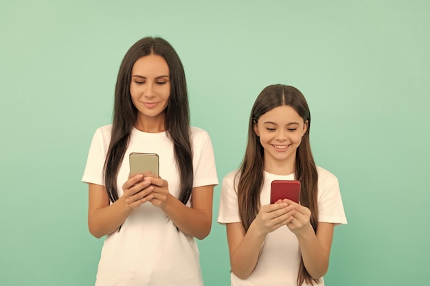 Feliz madre e hija charlando en el teléfono inteligente sobre fondo azul.