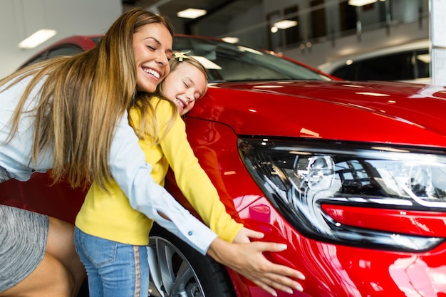 Feliz madre e hija comprando un coche nuevo en la sala de exposiciones de coches.