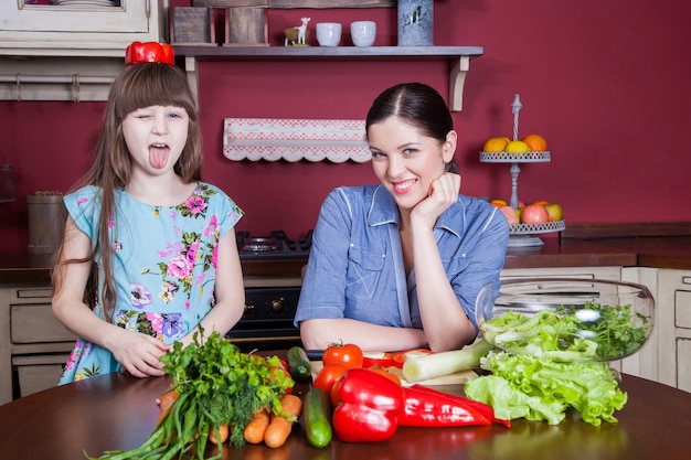Feliz madre e hija disfrutan haciendo y comiendo juntos en su cocina una comida saludable. hacen ensalada de verduras y se divierten juntos. Mamá cuida a su hija y le enseña a cocinar.