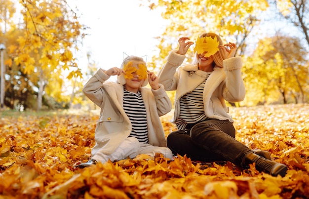 Feliz madre e hija se divierten en el parque de otoño al atardecer Familia en caminata Paseos infantiles descanso