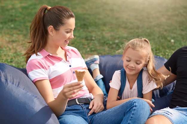 Feliz madre e hija divirtiéndose y jugando al aire libre, enviando tiempo libre juntos en la naturaleza, comiendo helado