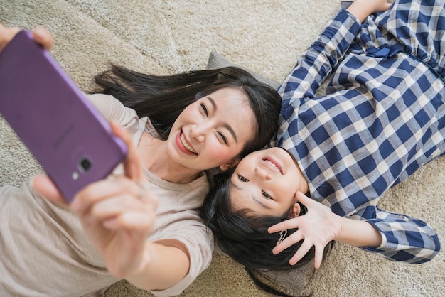 Feliz madre e hija de la familia asiática haciendo una foto selfie mientras se usa en el fondo de la sala de estar