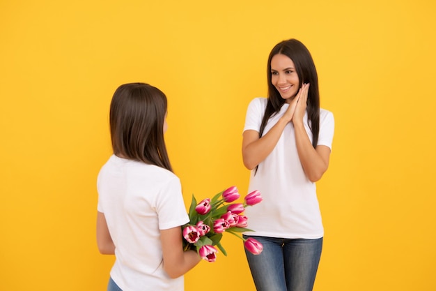 Feliz madre e hija con flores de tulipán sobre fondo amarillo primavera