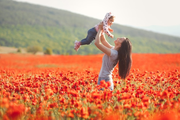 Feliz madre e hija jugando juntos y divirtiéndose en el campo de amapolas caminando en la naturaleza