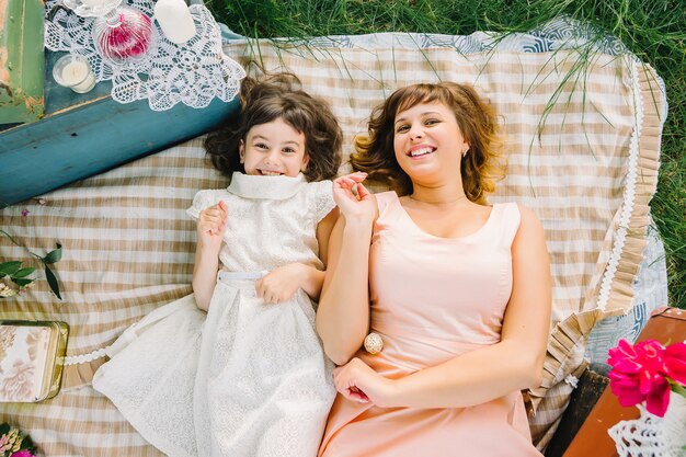 Feliz madre e hija jugando y sonriendo mientras está acostado sobre una manta en el verano