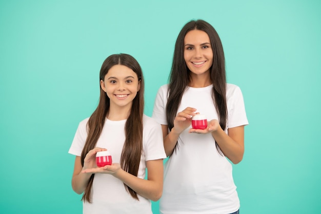 Feliz madre e hija niña sostienen frasco cosmético con producto de belleza en manos crema para la piel