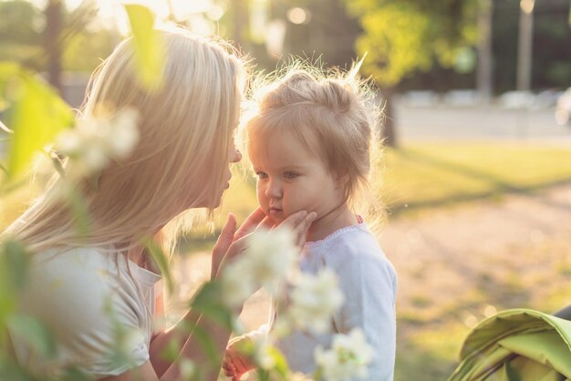 Feliz madre e hija pequeña en el parque en un día soleado al atardecer Mamá y niño al aire libre Concepto de ternura familia madre soltera flores sonrisas abrazos salud mental armonía vacaciones