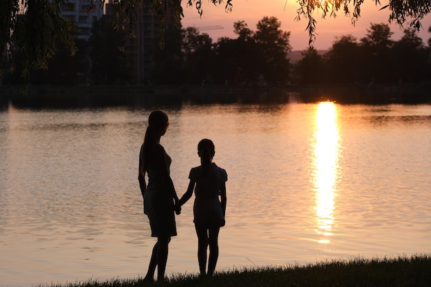 Feliz madre e hija de pie juntas cogidas de la mano disfrutando del tiempo en el parque de verano por la noche Concepto de relación y amor familiar