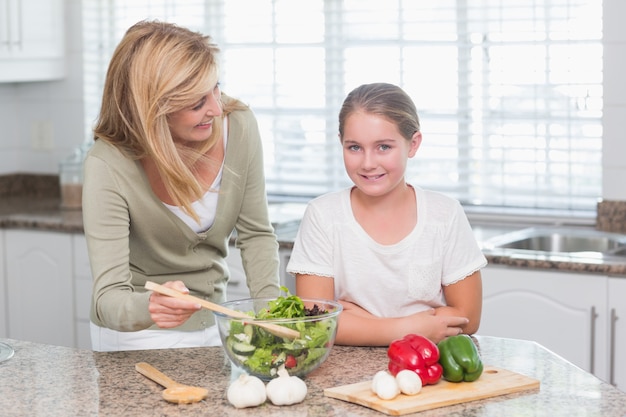 Feliz madre e hija preparando ensalada juntos