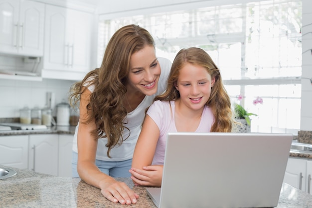 Feliz madre e hija usando la computadora portátil en la cocina