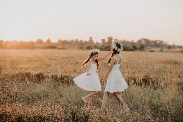 Feliz madre e hija vestidas de blanco están girando y tienen alegría y felicidad en verano