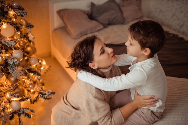 Feliz madre e hijo en casa en el dormitorio cerca del árbol de Navidad