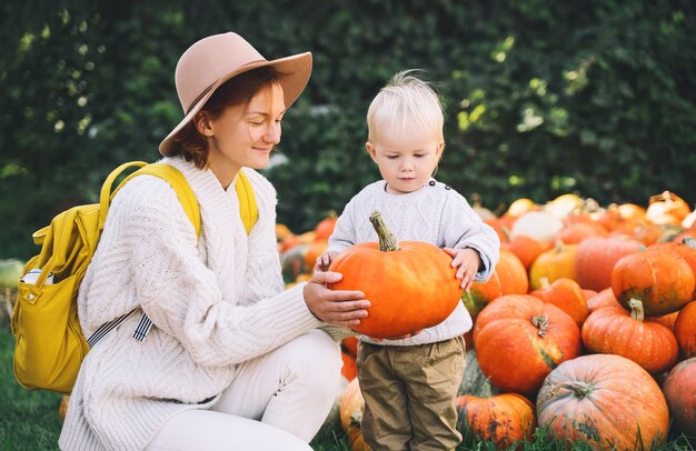 Feliz madre e hijo en el huerto de calabazas al aire libre mujer y niño jugando en la granja