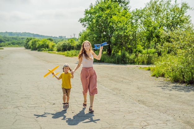 Feliz madre e hijo jugando con un avión de juguete contra el antiguo fondo de la pista Viajando con el concepto de niños