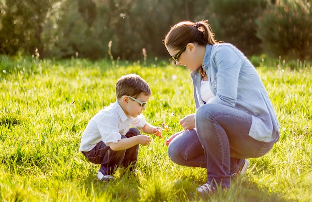 Feliz madre e hijo lindo recogiendo un ramo de flores en un campo soleado