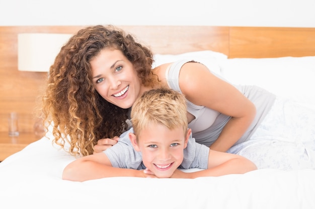 Feliz madre e hijo posando en la cama mirando a cámara